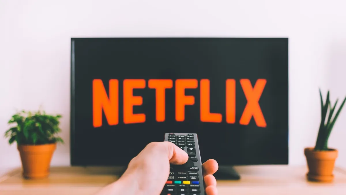 A hand pointing a remote control at a television showing a streaming service