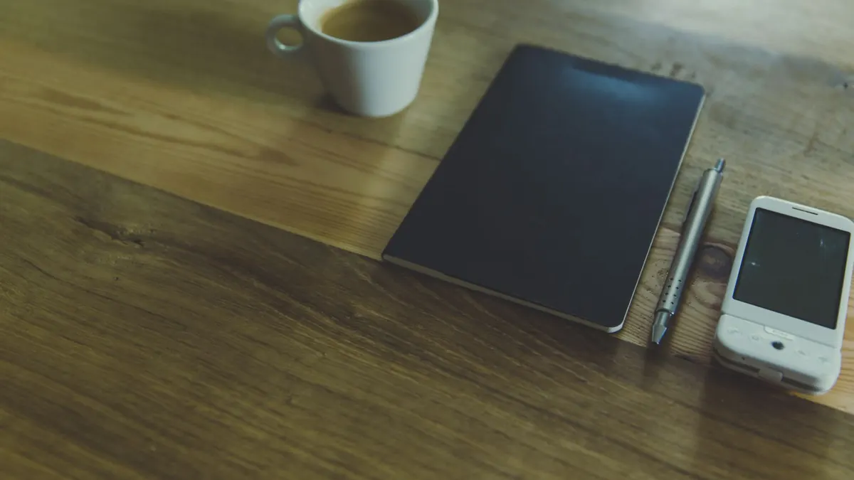 A smartphone, a notebook and a cup of coffee on a wooden table