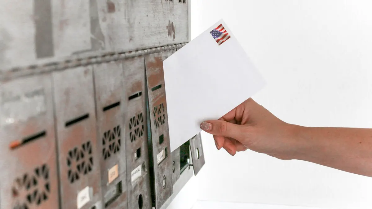 A hand posting a white envelope into a row of vintage letterboxes