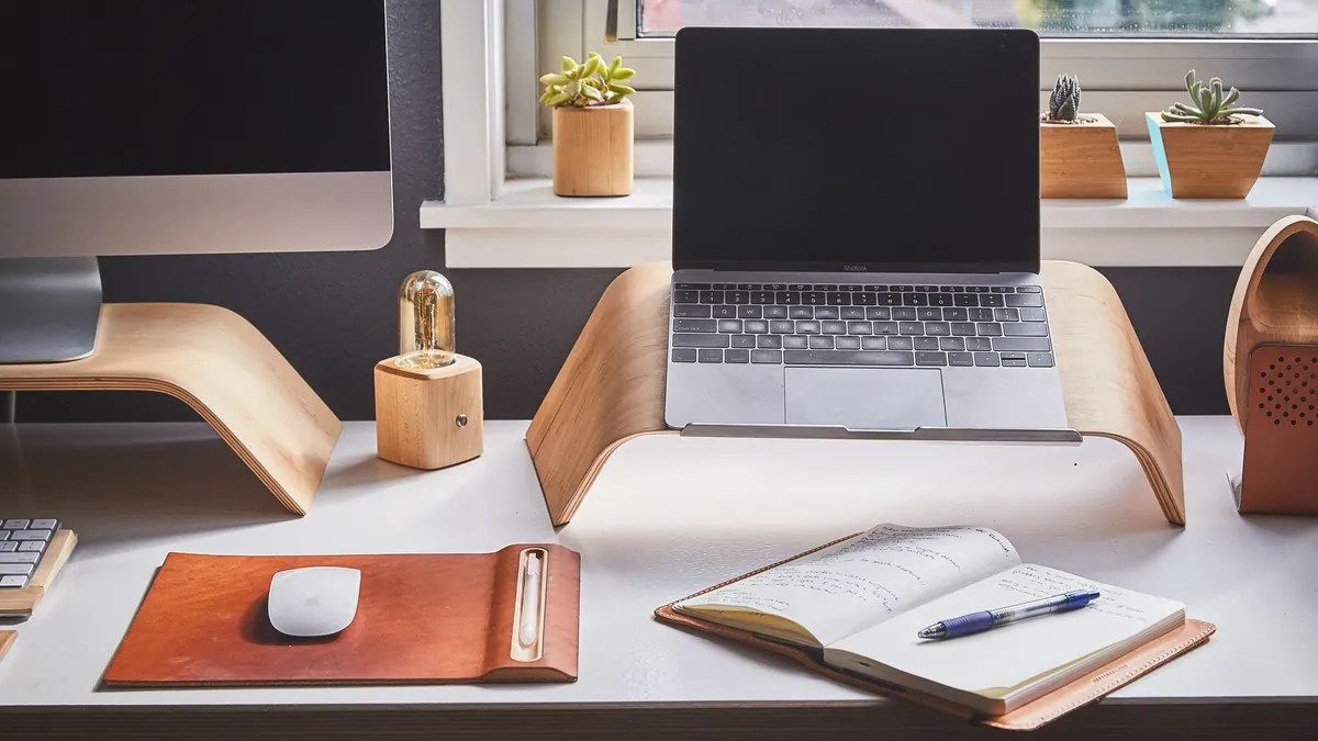 A laptop on a wooden stand at a tidy desk by a window