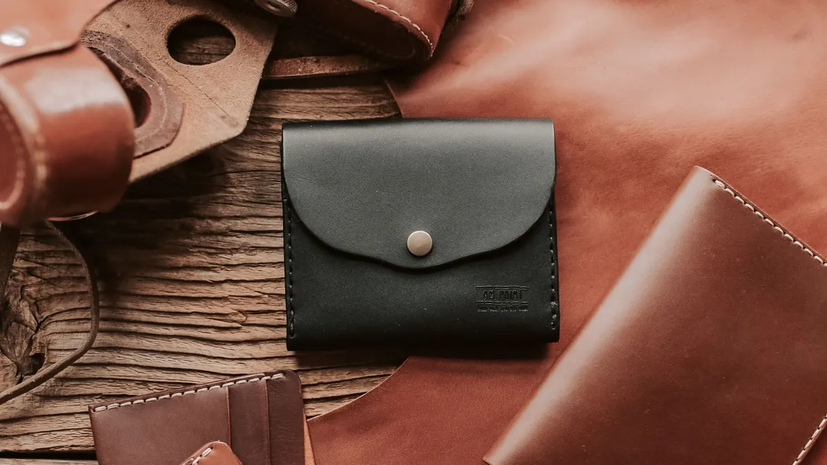 A small dark leather wallet on a wooden table beside a leather bag