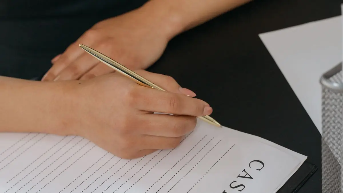 A hand signing a document with a pen