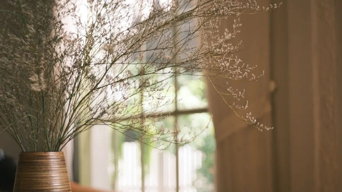 Dried wildflowers in a vase beside a sunlit window