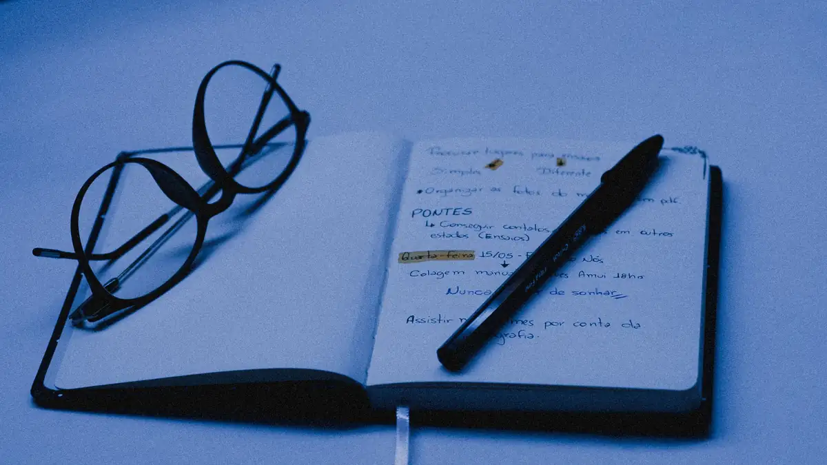 An open notebook with a pen and a pair of glasses on a desk
