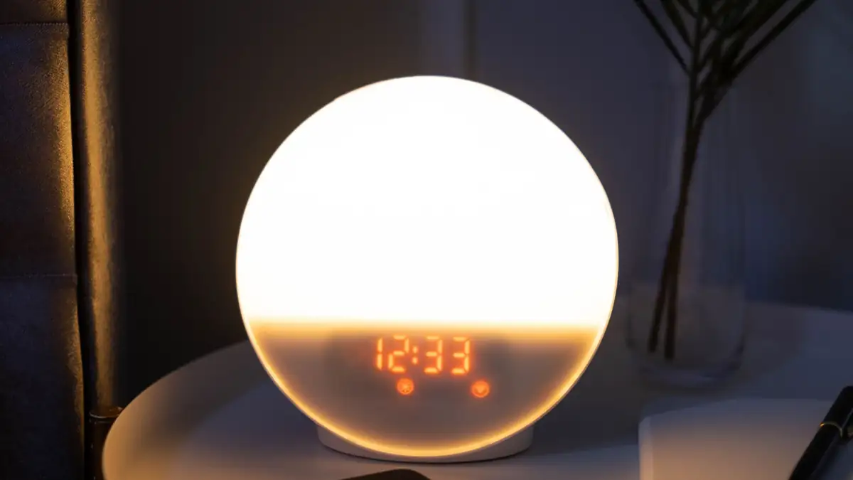 A bedside table at night with a glowing alarm clock and a phone