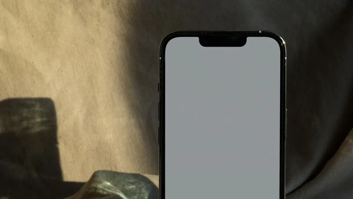 A smartphone resting on a paper-toned surface in soft shadow